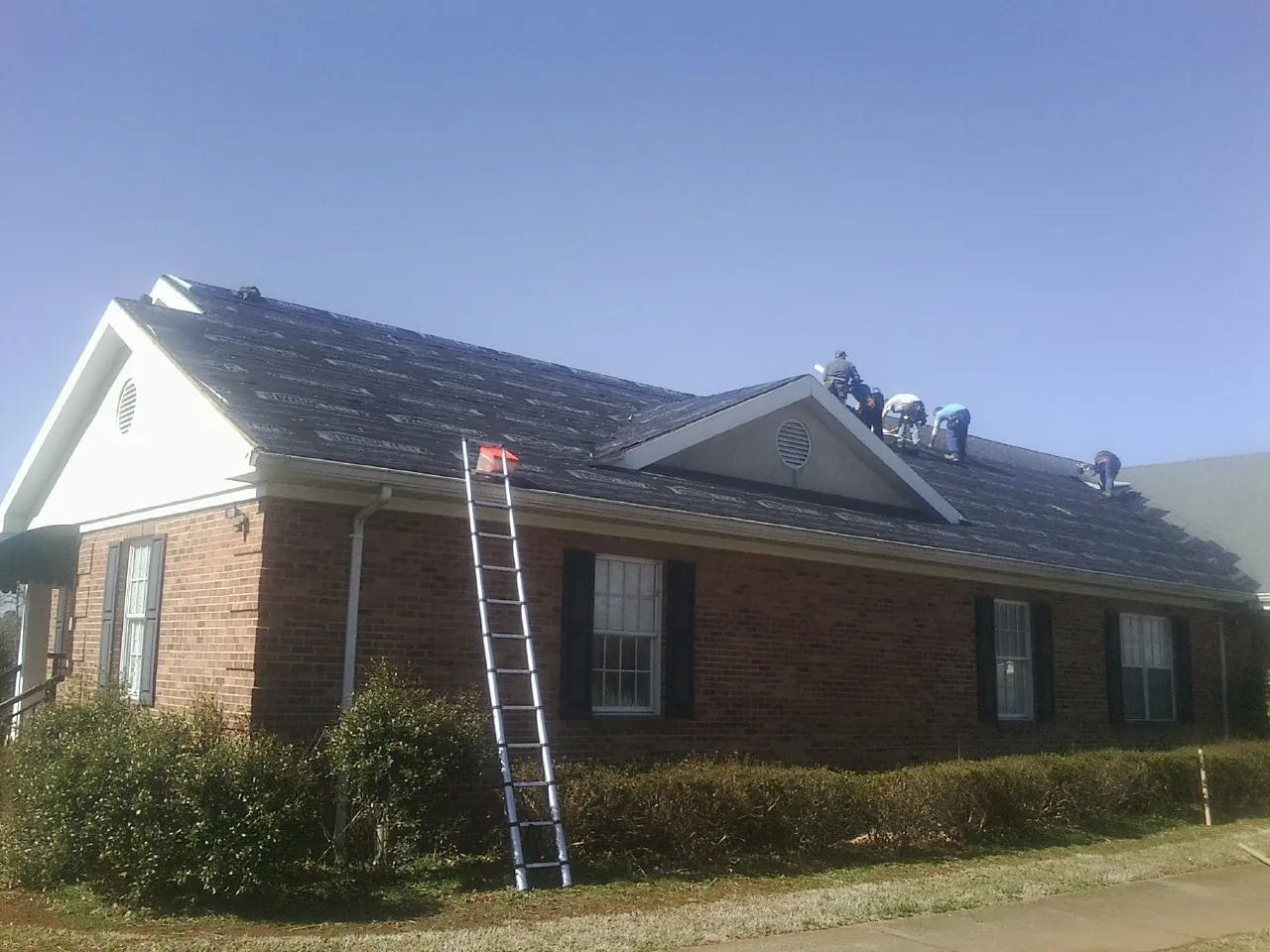 Crew tearing shingles off a brick ranch roof with a ladder set — Emergency Roof Repair work by our crew in Kimberton