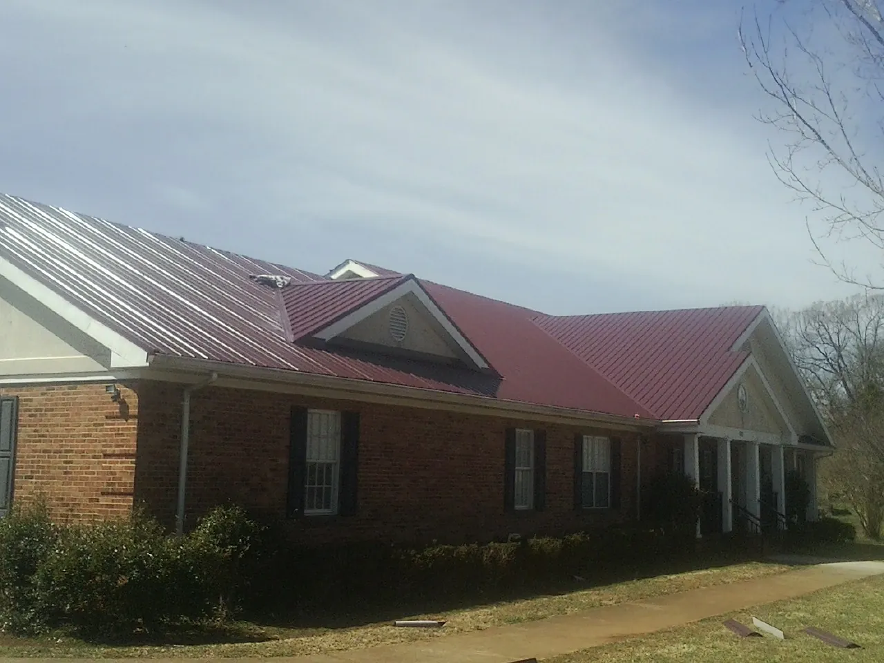 Red metal roof with gabled entries on a long brick building, from a Hail Damage Roof Repair job in Kimberton
