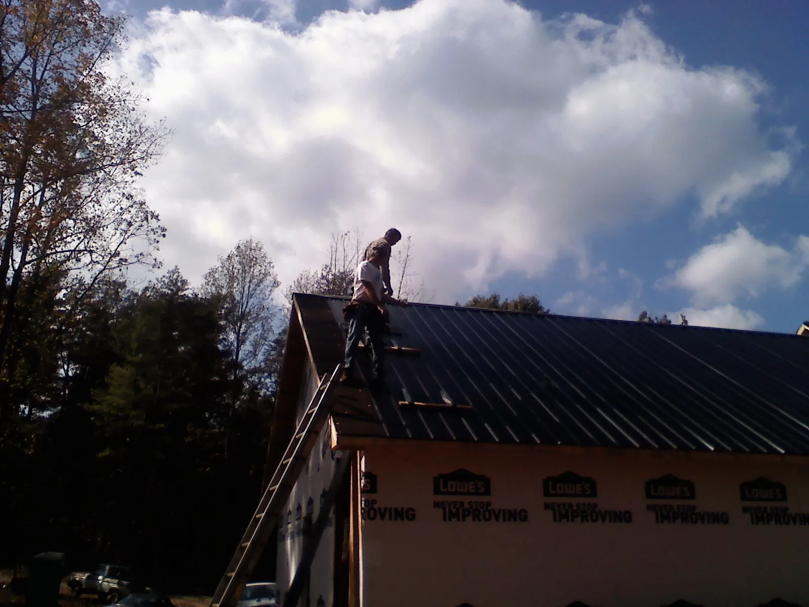 Roofer fastening dark metal panels high against a cloudy sky, from a Roof Inspection job in Kimberton