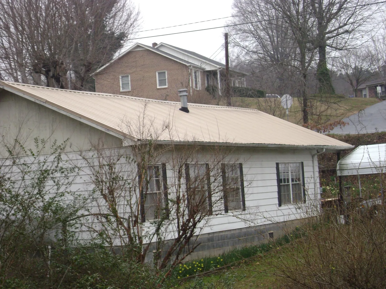 Tan metal roof on a white sided house set into a hillside — Commercial Roofing by Roofing Brothers in Kimberton